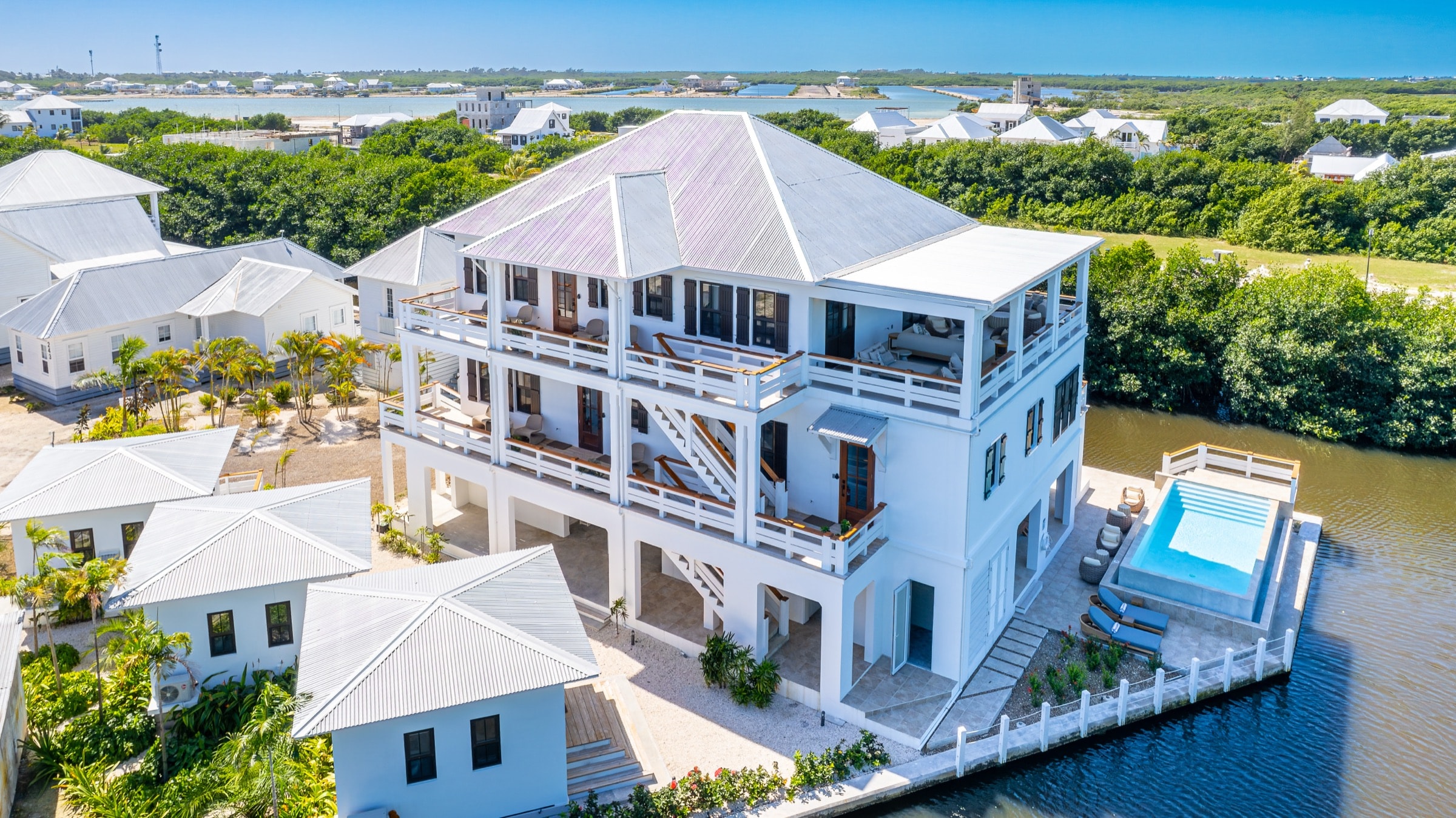 Aerial view of the full BelaDia three-story waterfront compound, infinity pool, and private dock inside Mahogany Bay Village